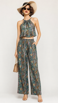 A woman models a matching two-piece set featuring an EVERSHE sleeveless halter crop top and wide-leg pants in a teal and orange paisley pattern, styled with a beige wide-brim hat, sunglasses, and a small beige handbag against a light gray studio background.