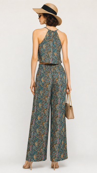 A woman modeling an EVERSHE sleeveless halter-neck jumpsuit with wide legs, shown from the back. The jumpsuit has an intricate multicolor paisley pattern in teal, green, and gold tones.