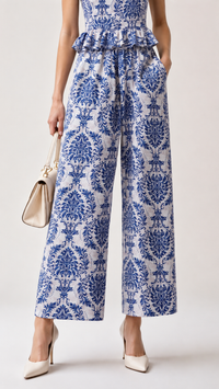 A model wearing an EVERSHE blue and white damask patterned wide-leg cropped pants with a ruffled waist, paired with cream high heels and holding a small beige handbag, against a light gray studio background.